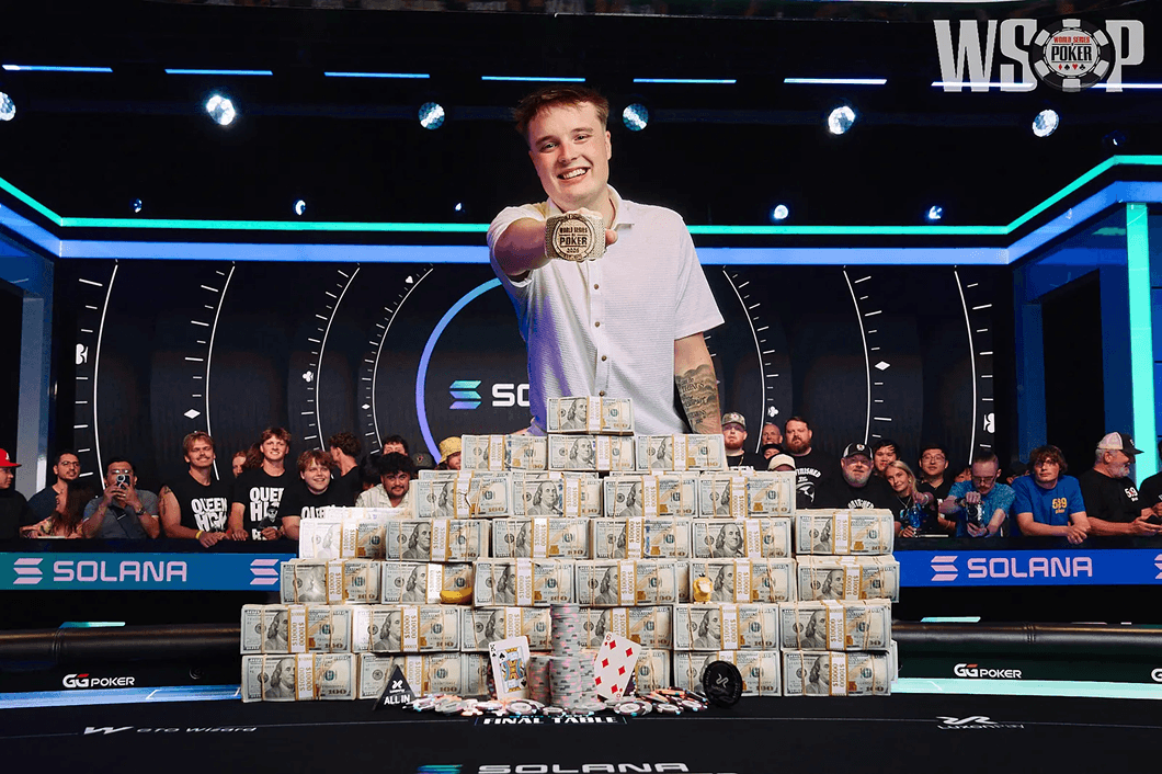 A 2026 WSOP champion holds up his bracelet behind stacks of prize money.